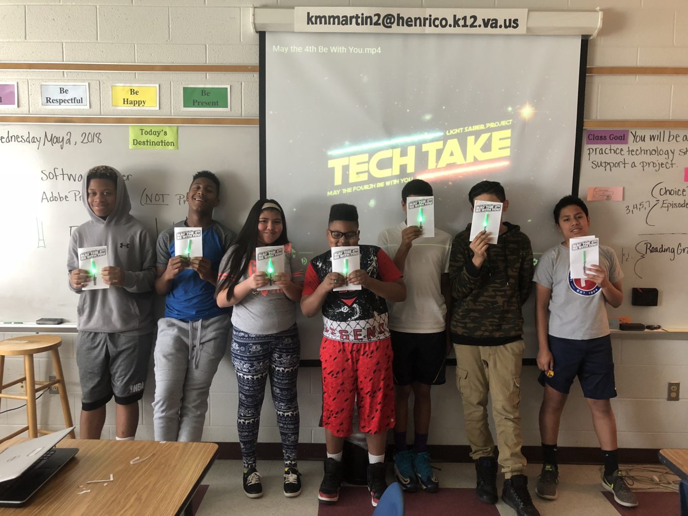 Seven students holding finished paper circuit lightsabers at the front of a classroom.